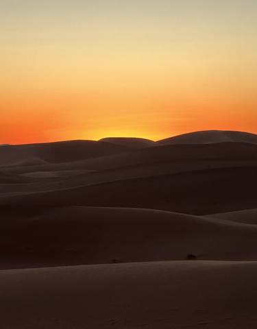 Desert dunes silhouetted against a vibrant sunset.