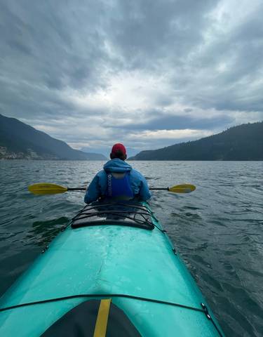 Person kayaking on a lake with mountains in the distance under an overcast sky.