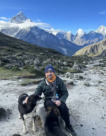 Person sitting with a dog, with mountains in the background.