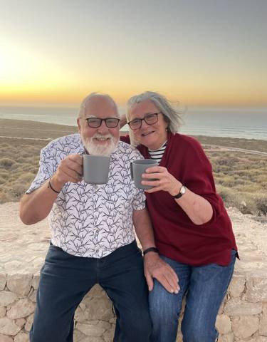 A smiling couple holding mugs with a scenic view in the background.