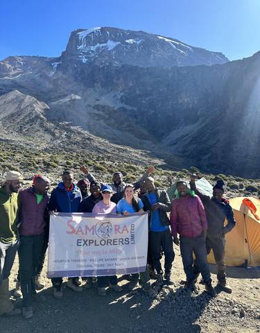 A group of hikers posing with a banner in a mountainous area.