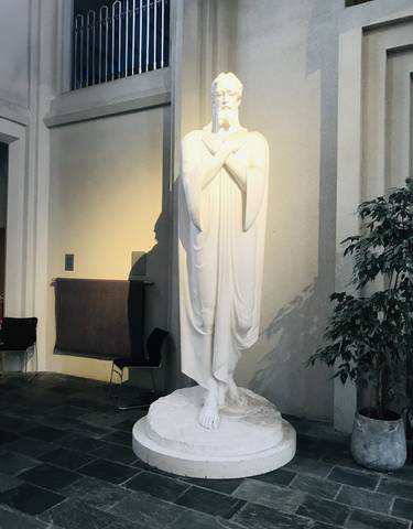 A white statue inside a building, next to a plant.
