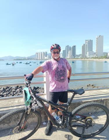 Cyclist posing near a waterfront with high-rise buildings.