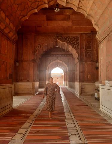 Person standing inside a historic building with arches and intricate designs.
