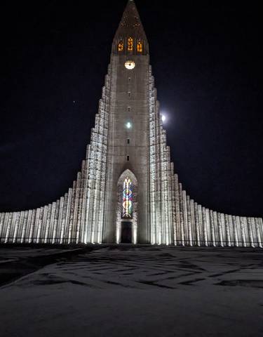 Night view of the illuminated Hallgrimskirkja with moon visible.