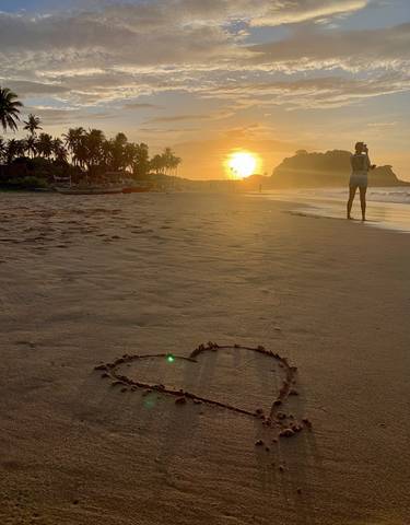 A heart drawn in the sand on a beach during a glowing sunset.