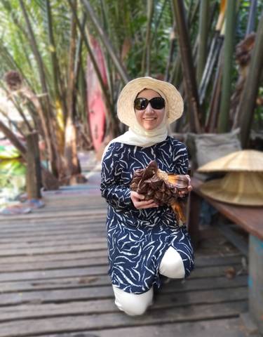 A woman in a sunhat holding a flower bouquet, posing outdoors.