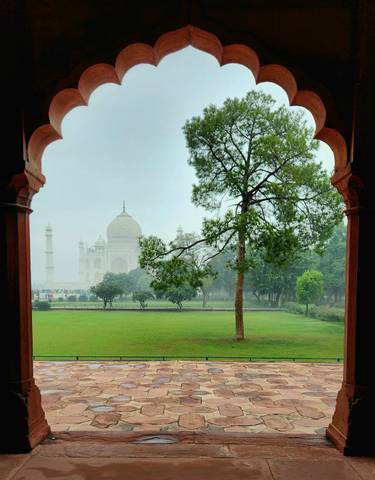 Taj Mahal viewed through a beautifully arched window with green gardens.
