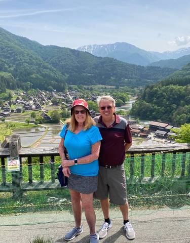 Two people overlooking a traditional Japanese village from a high vantage point.