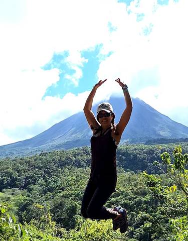 Person posing with the backdrop of a volcano.
