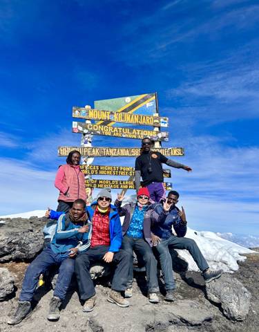 Group of people posing at the summit of Mount Kilimanjaro.