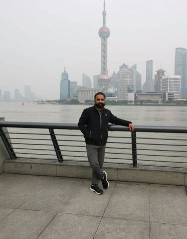Person standing by a riverside with a cityscape in the background.