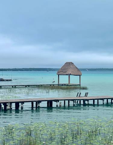 Wooden jetty leading into a turquoise lake with a thatched hut.