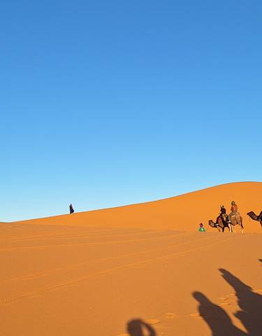 Group of people riding camels on sand dunes in the desert.