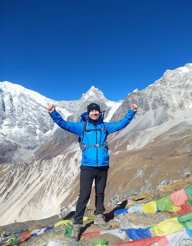 A man posing triumphantly in a mountain landscape.