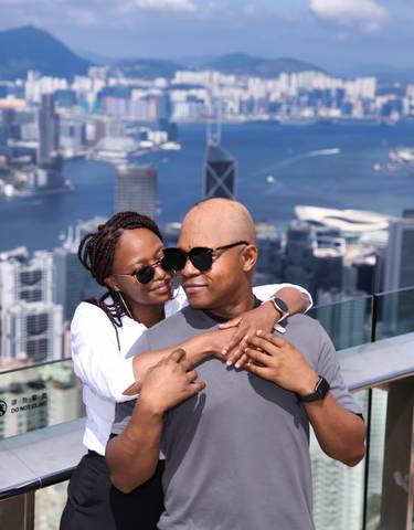 Couple posing on a glass balcony with a city skyline in the background.