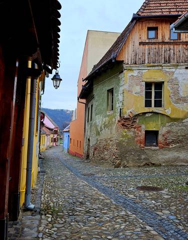 Narrow cobblestone street between colorful old buildings with a view of distant hills.