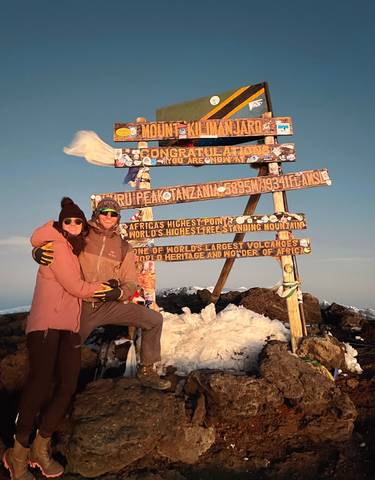 Couple embracing in front of a summit sign with snow around.
