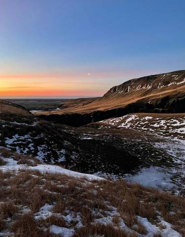 Scenic valley with snowy patches and a sunset.