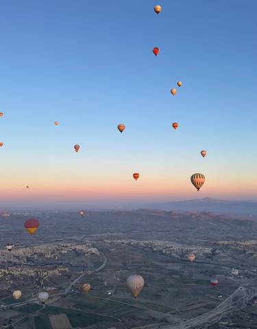 Numerous hot air balloons floating in a clear sky over a scenic landscape.