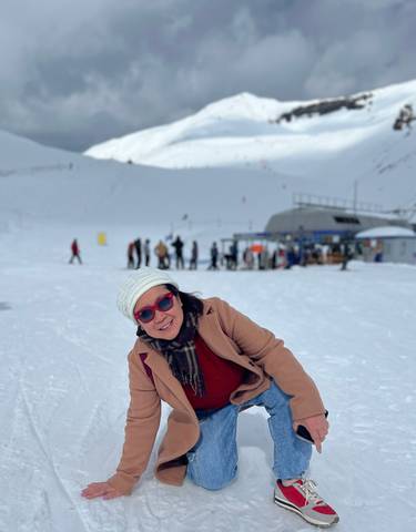 Woman in winter attire on a snowy landscape, with people in the background.