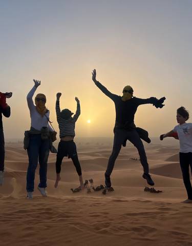 Group of people jumping in the desert at sunrise.