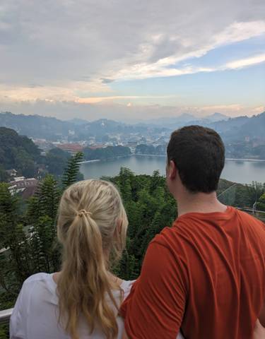 Two people overlooking a cityscape with a lake and hills.