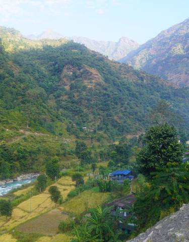 A scenic view of a valley with a river, fields, and houses, surrounded by mountains.