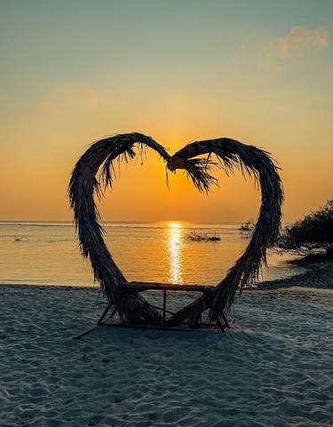 Heart-shaped palm decoration on beach during sunset.