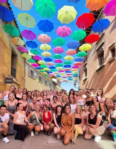 Large group of people posing under colorful umbrellas in a street.