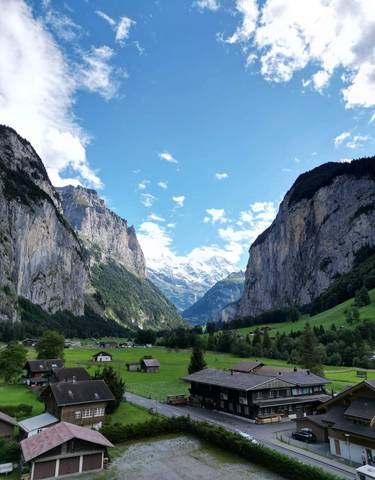 View of a majestic valley with high cliffs, a green landscape, and snow-capped mountains.