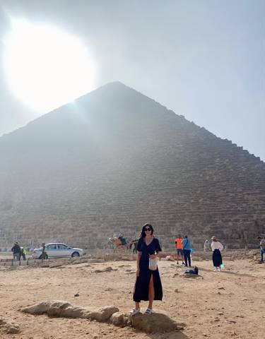 Person in front of a large pyramid with sunlight filtering through.