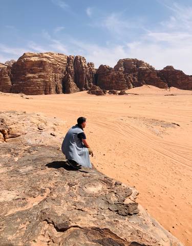 A person sitting on a rock in a desert landscape with rocky formations.
