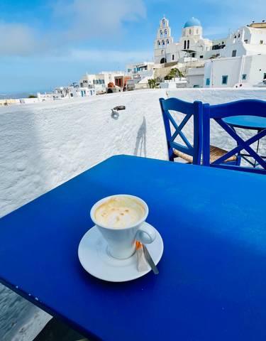 A cup of coffee on a blue table with matching blue chairs outside a white building.