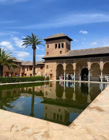 People visiting a historic Moorish palace with a reflection pool.