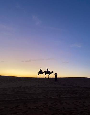 Silhouettes of people on camels at sunset.