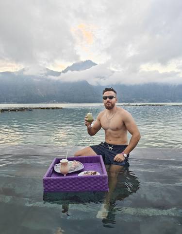 Person sitting in an infinity pool with a drink, overlooking mountains.