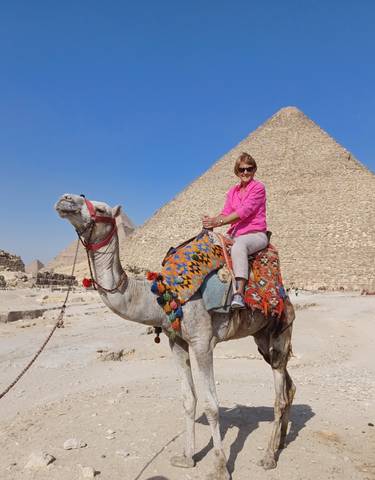 A person riding a camel in front of the pyramids in Egypt.