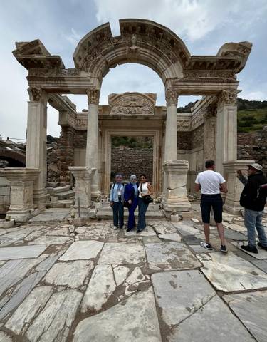 Three women and a man stand in front of ancient Roman-style ruins with columns.