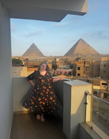 A woman standing on a balcony with pyramids in the background.