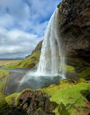 Waterfall with a rainbow in a lush green landscape.
