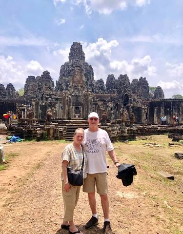 Couple posed in front of the Bayon Temple, an ancient stone structure.