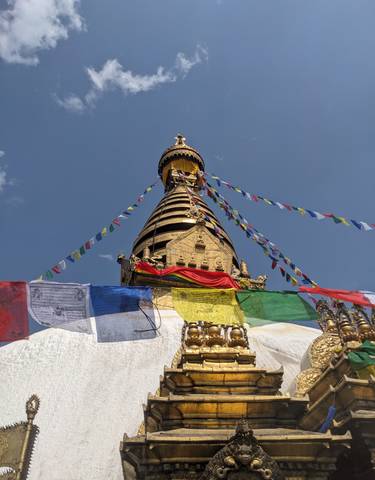 Stupa with prayer flags against a blue sky.