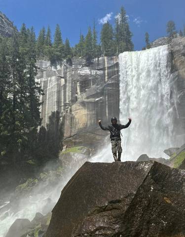 Person posing triumphantly in front of a waterfall.