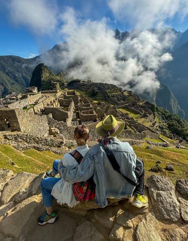 Couple sitting and admiring Machu Picchu ruins with clouds around.