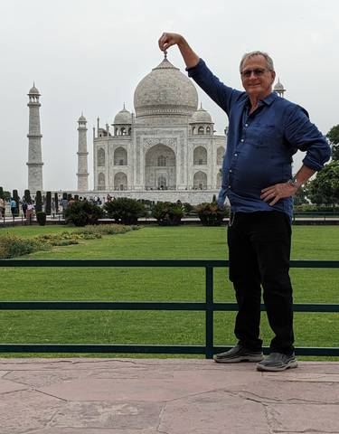 A man posing in front of the Taj Mahal with lush gardens.