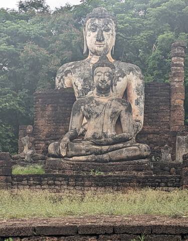 Ancient stone Buddha statue amidst ruins with greenery.