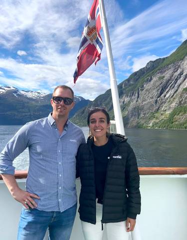 Two people posing on a boat with fjords in the background.
