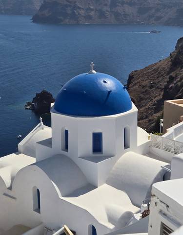 Blue-domed church with a view of the sea and rocky coastline.