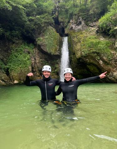 Couple in wetsuits posing in front of a waterfall.